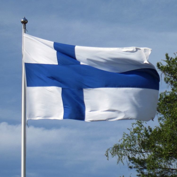 Suomen lippu liehuu sinistä taivasta vasten.