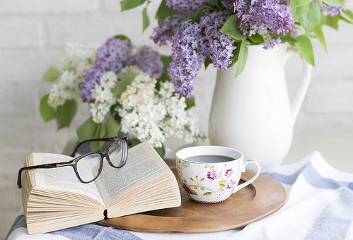 Kahvikuppi, silmälasit ja kukkia maljakossa.