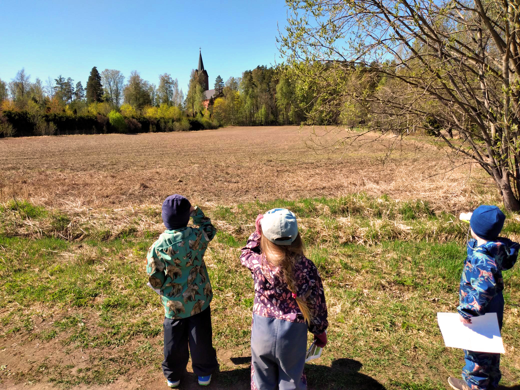 Kolme lasta kiikaroivat pellon poikki Mäntsälän kirkkoa.