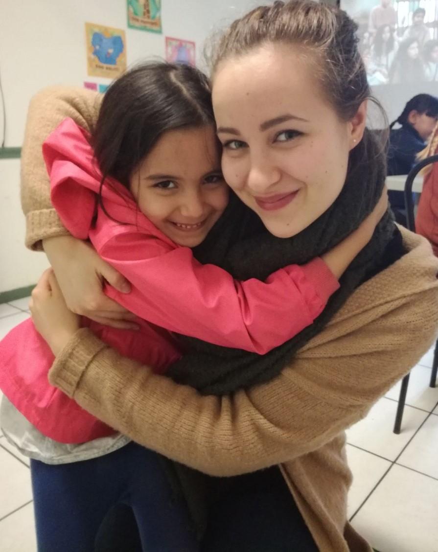 Nuori tyttö ja pakolaistyttö halaavat toisiaan, katsovat kameraan ja hymyilevät