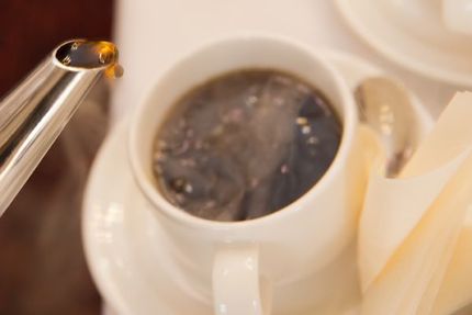 Kahvipannun nopkasta valuu kahvipisara kohti alla näkyvää valkoista kahvikuppia, jossa on jo kahvia.